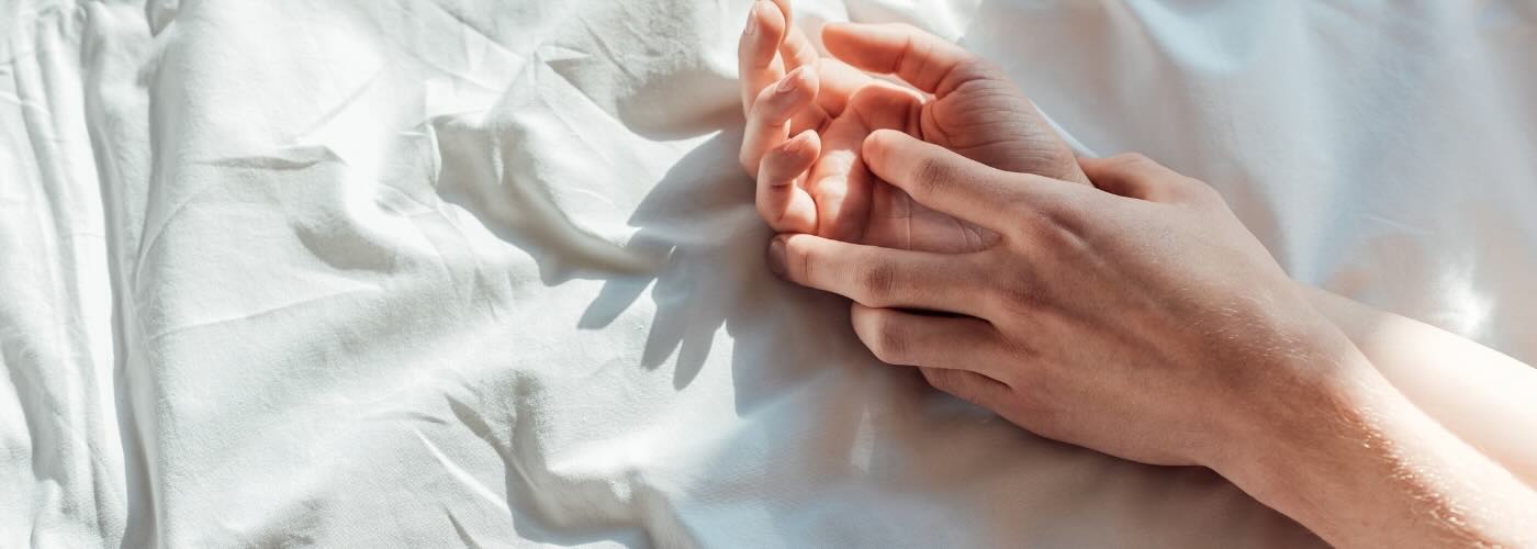 Couple holding hands on white sheets